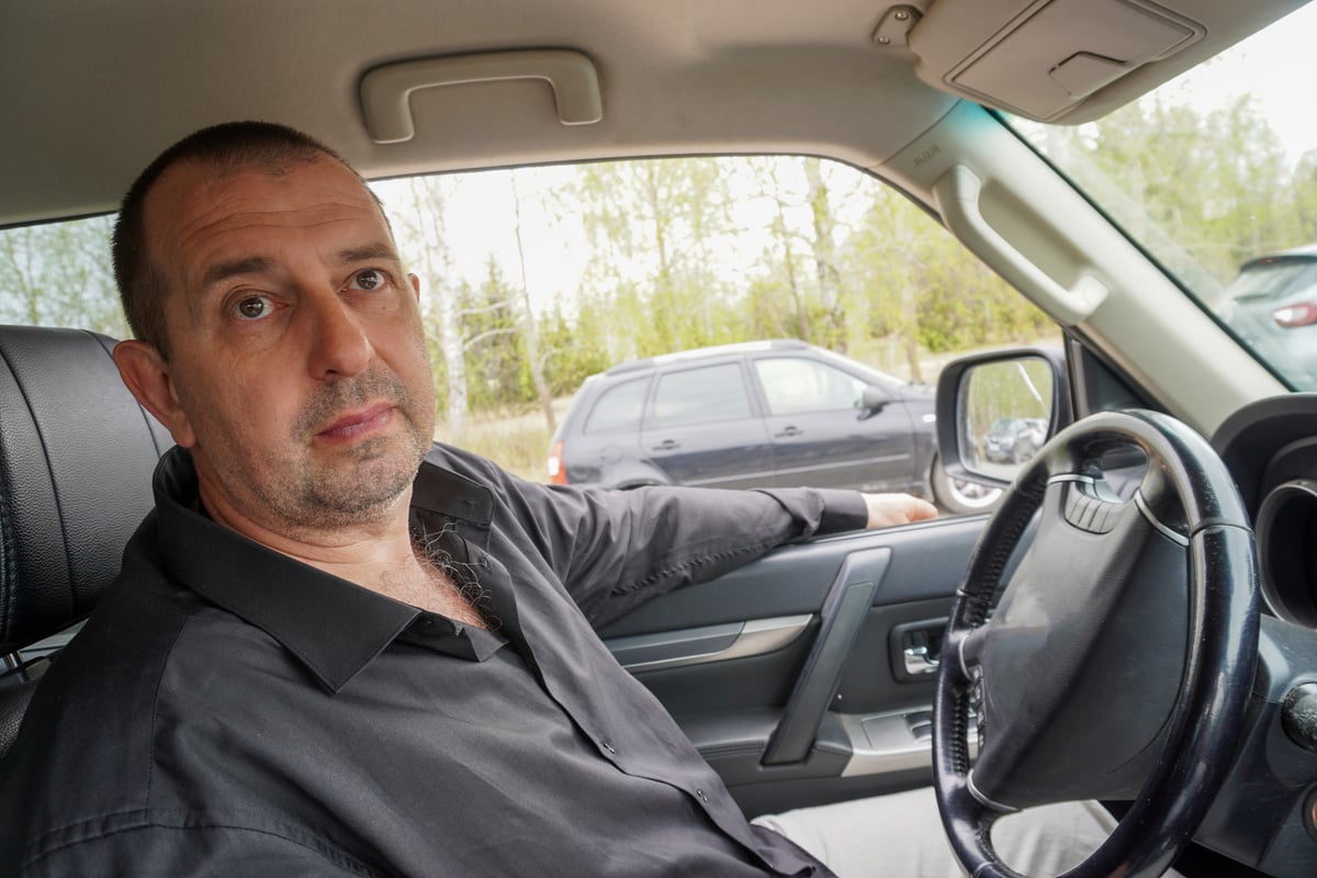 Man 50 years old in a black shirt driving a car